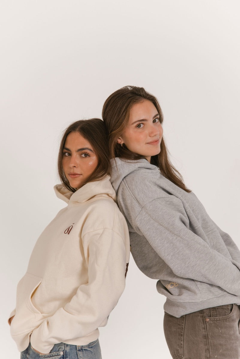 Dos amigas espalda con espalda con hoodies crema y gris